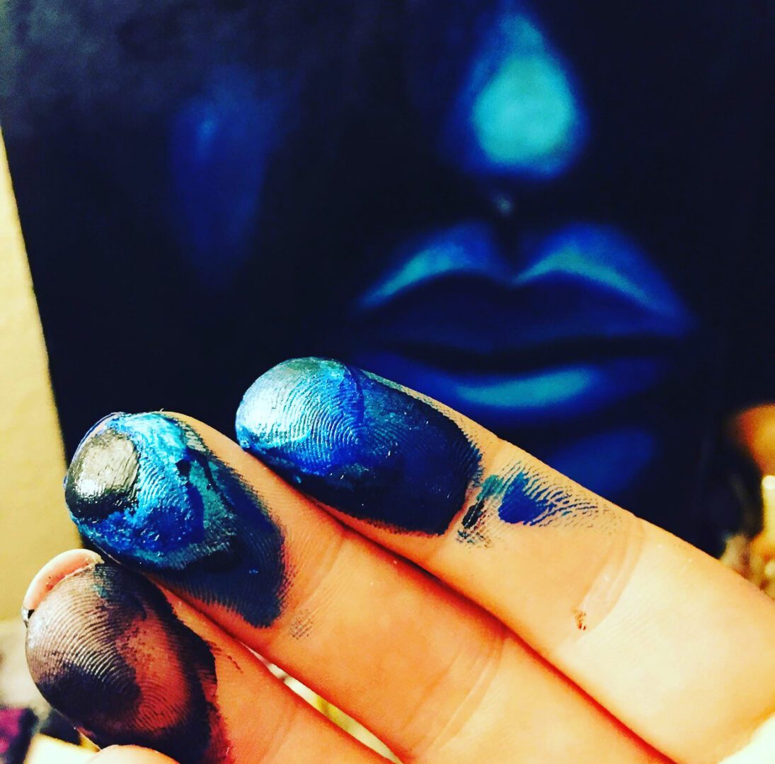 Close-up of hands and face covered in vibrant blue paint.