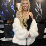 A woman with long blonde hair wearing a white fur coat and black dress.